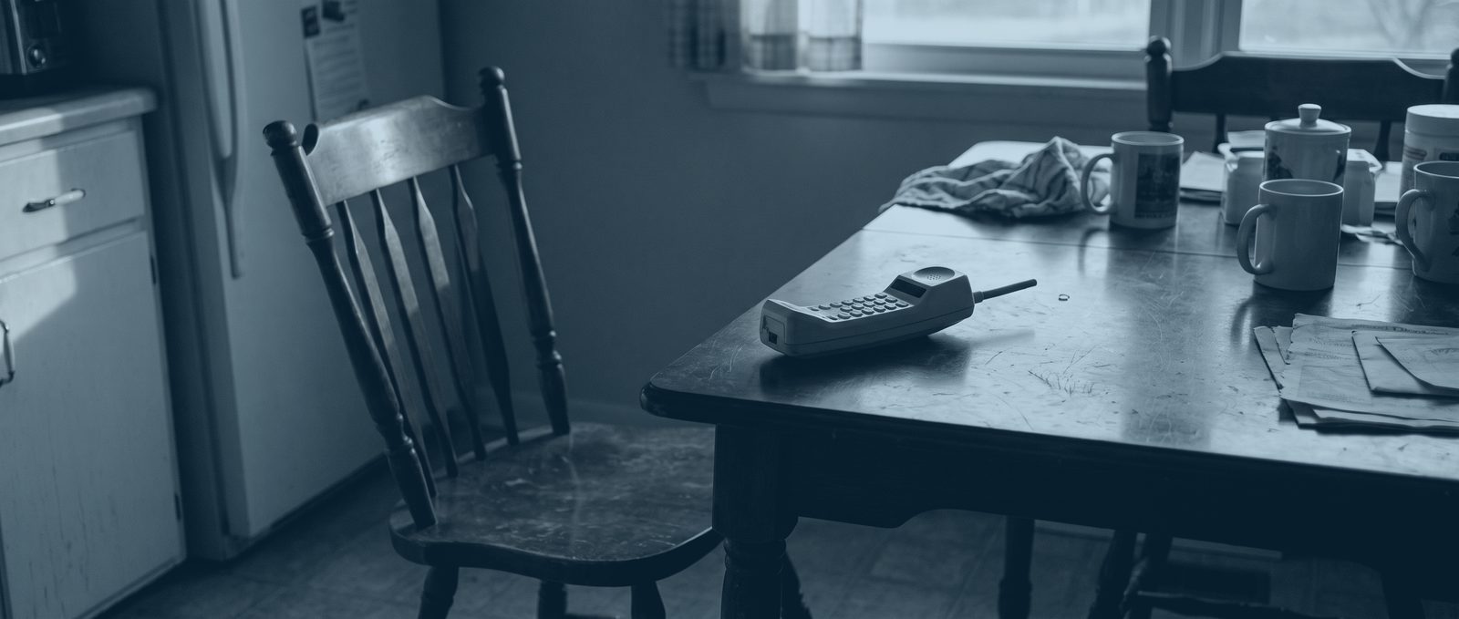 A cordless telephone handset lying on a kitchen table in an empty room, late in the day.